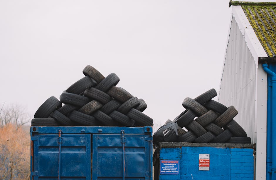 A pair of large blue industrial containers filled with stacked used rubber tyres, primarily black with some showing slight wear and dirt. The tyres vary in size and are arranged in a somewhat haphazar